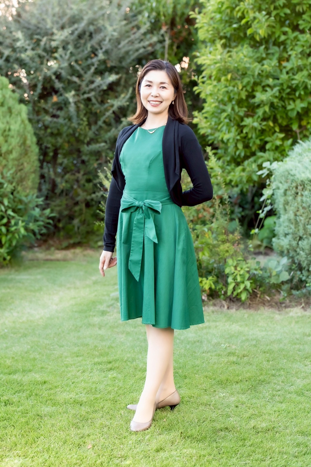 緑のワンピースドレスを着た千原輝子が庭園で立つ姿 - 姿勢・声・表情・雰囲気が一体となった自然な佇まい